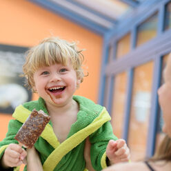 Ein Kind isst Eis im Wintergarten der Saunalandschaft und lächelt.
